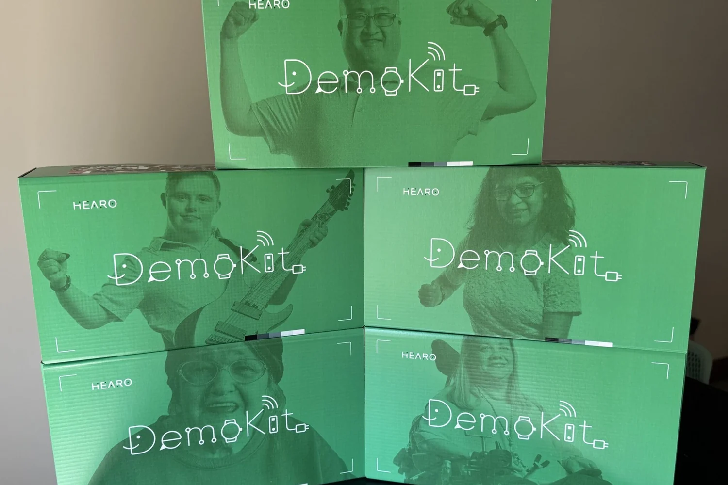 A tower of five Hearo Demo Kit boxes, each printed with a person who lives more independently with Hearo